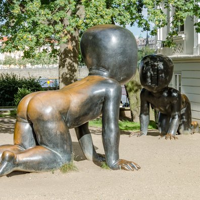 Drei riesige, krabbelnde Babys aus Bronze befinden sich im Park neben dem Museum Kampa. Ihre Gesichter sind durch eine Art Barcode oder Lüftungsschlitz entmenschlicht, was eine beunruhigende und nachdenkliche Wirkung erzeugt. Sie sind identisch mit den Babys, die am Fernsehturm in Žižkov empor krabbeln. Die Skulpturen laden zum Klettern ein, werfen aber gleichzeitig Fragen zur Zukunft, Identität und Dehumanisierung in der modernen Welt auf.